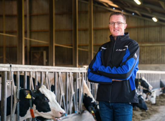 Melkveehouder Martin Brandsma met DeLaval jas in de stal met voerhek en koeien op de achtergrond